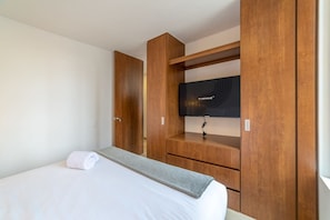 A hotel room with a bed, a TV on a wooden stand, and a wardrobe.