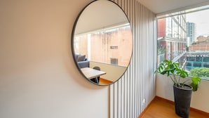 A modern room with a large round mirror, a potted plant, and a view of the city through a large window.