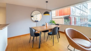 A modern dining area with a wooden table, black chairs, a round mirror, and a pendant light.