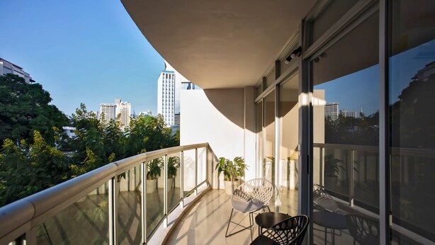 A balcony with a glass railing, a table, two chairs, and potted plants. - Modern 2BR In La Cresta (Panama City)