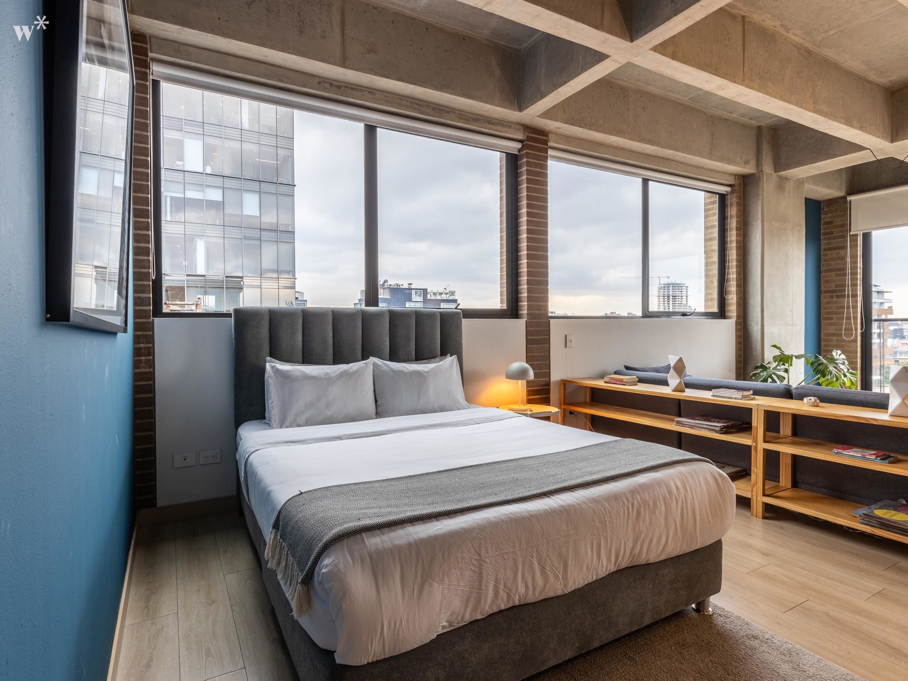 Ein modernes Schlafzimmer mit einem großen Bett, einem Schreibtisch und Blick auf die Stadt.