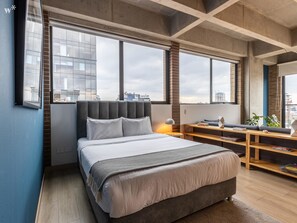 A modern bedroom with a large bed, a desk, and a view of the city.