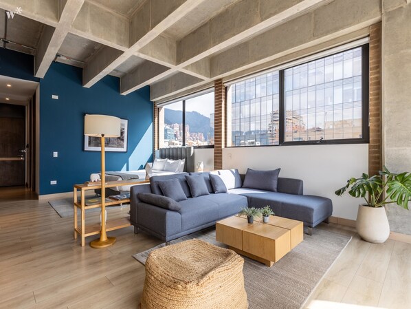 A modern living room with a sectional sofa, a coffee table, and a large window offering a city view.