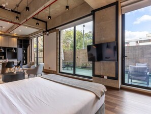 Una habitación de hotel moderna con una cama grande, un televisor montado en la pared y un balcón con mobiliario exterior.