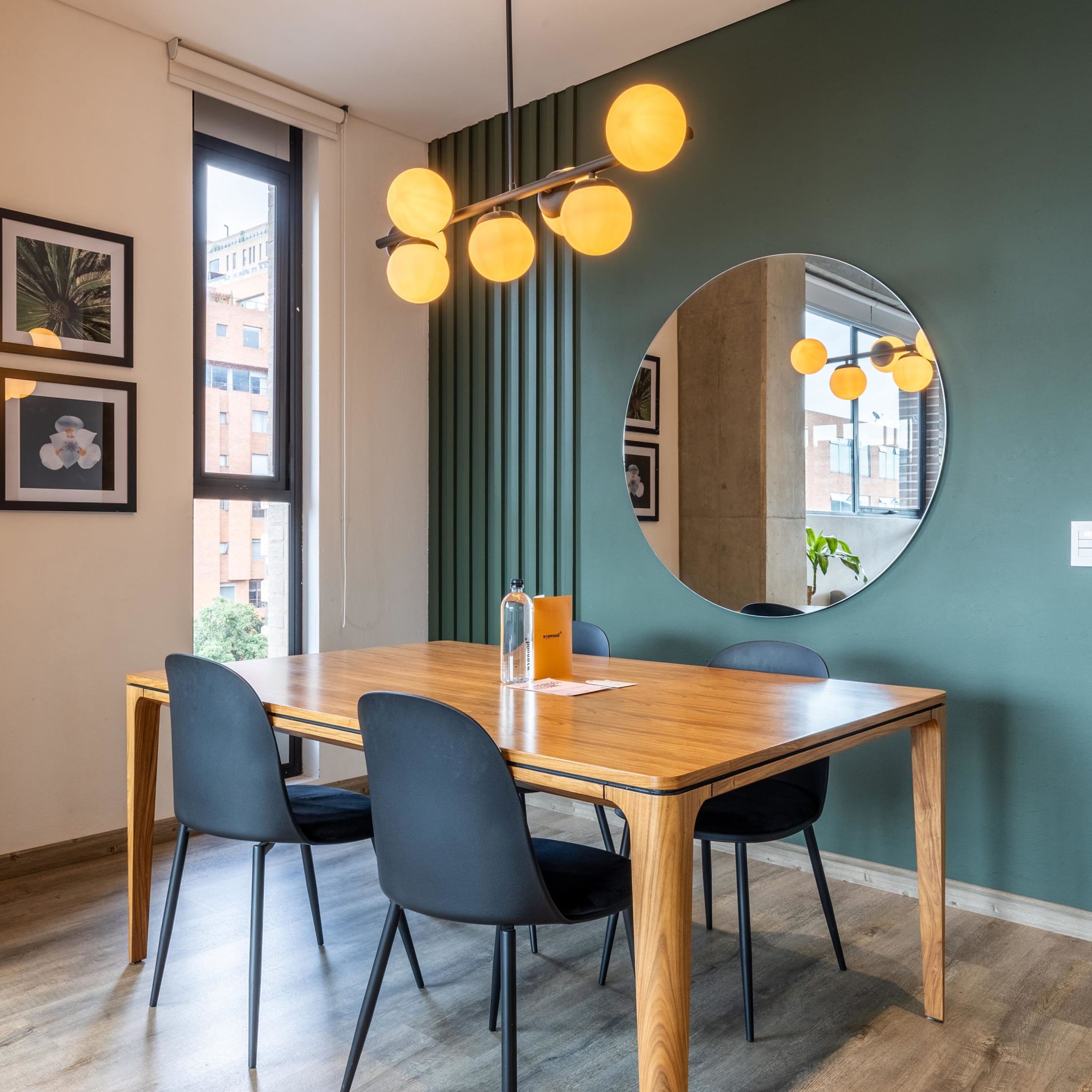 A dining area with a wooden table, black chairs, a round mirror, and a wall-mounted light fixture.