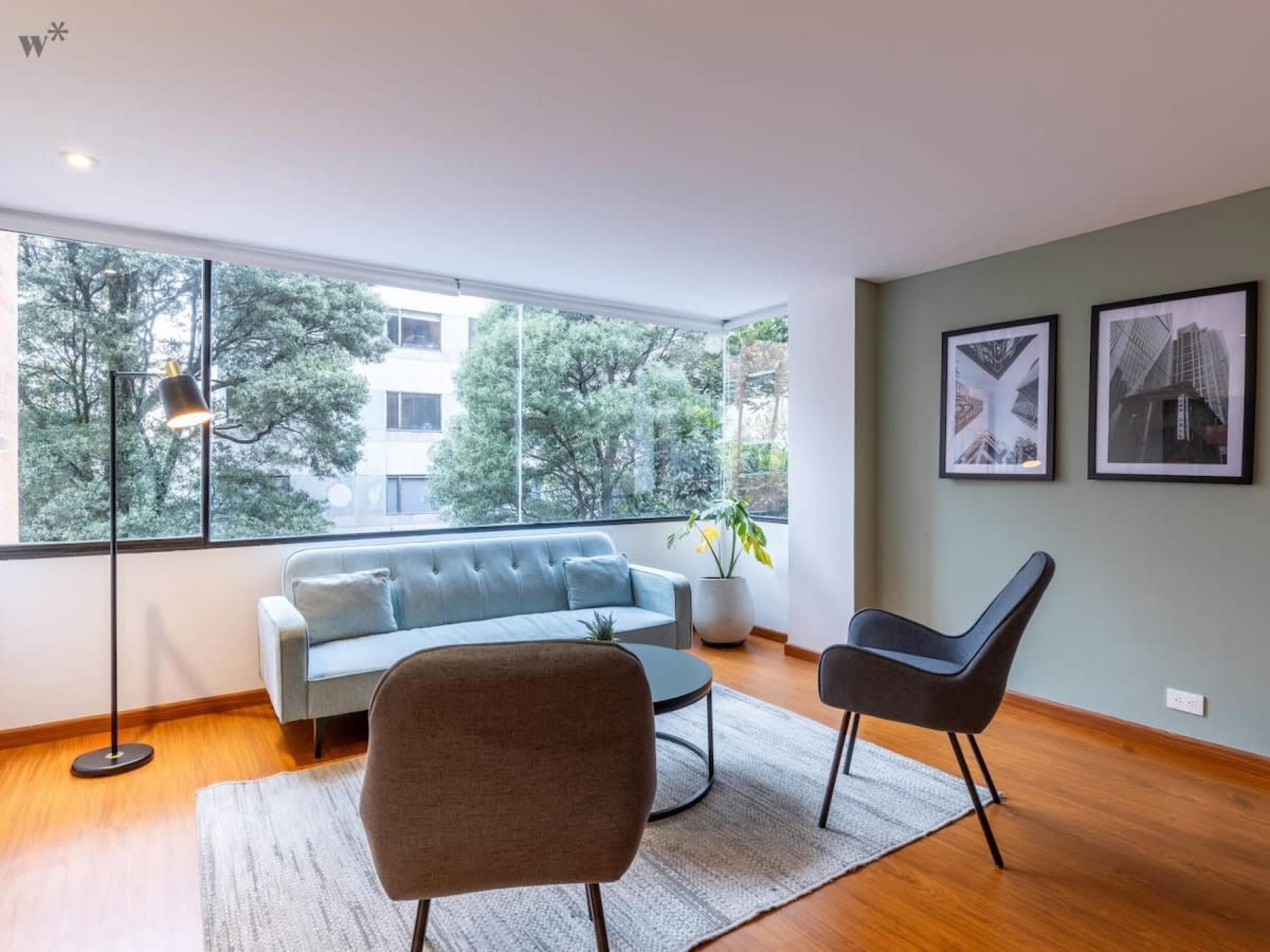 A modern living room with a sofa, two chairs, a coffee table, and a large window with a view of trees and buildings.
