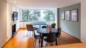 Uma sala de jantar moderna com uma mesa redonda, cadeiras pretas, um sofá e uma televisão em um móvel.