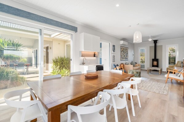 A spacious living area with a large wooden dining table, white chairs, a sofa, and a fireplace.