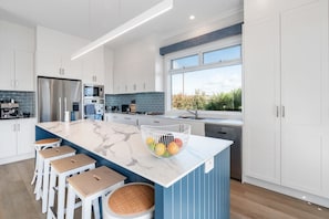 A modern kitchen with white cabinets, a marble island, and a large window.