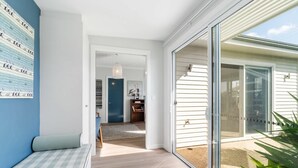 A modern interior with a checkered sofa, a hallway leading to a dark blue door, and a large sliding glass door to the outside. - 6 Beach Rd Goolwa South (Goolwa South)