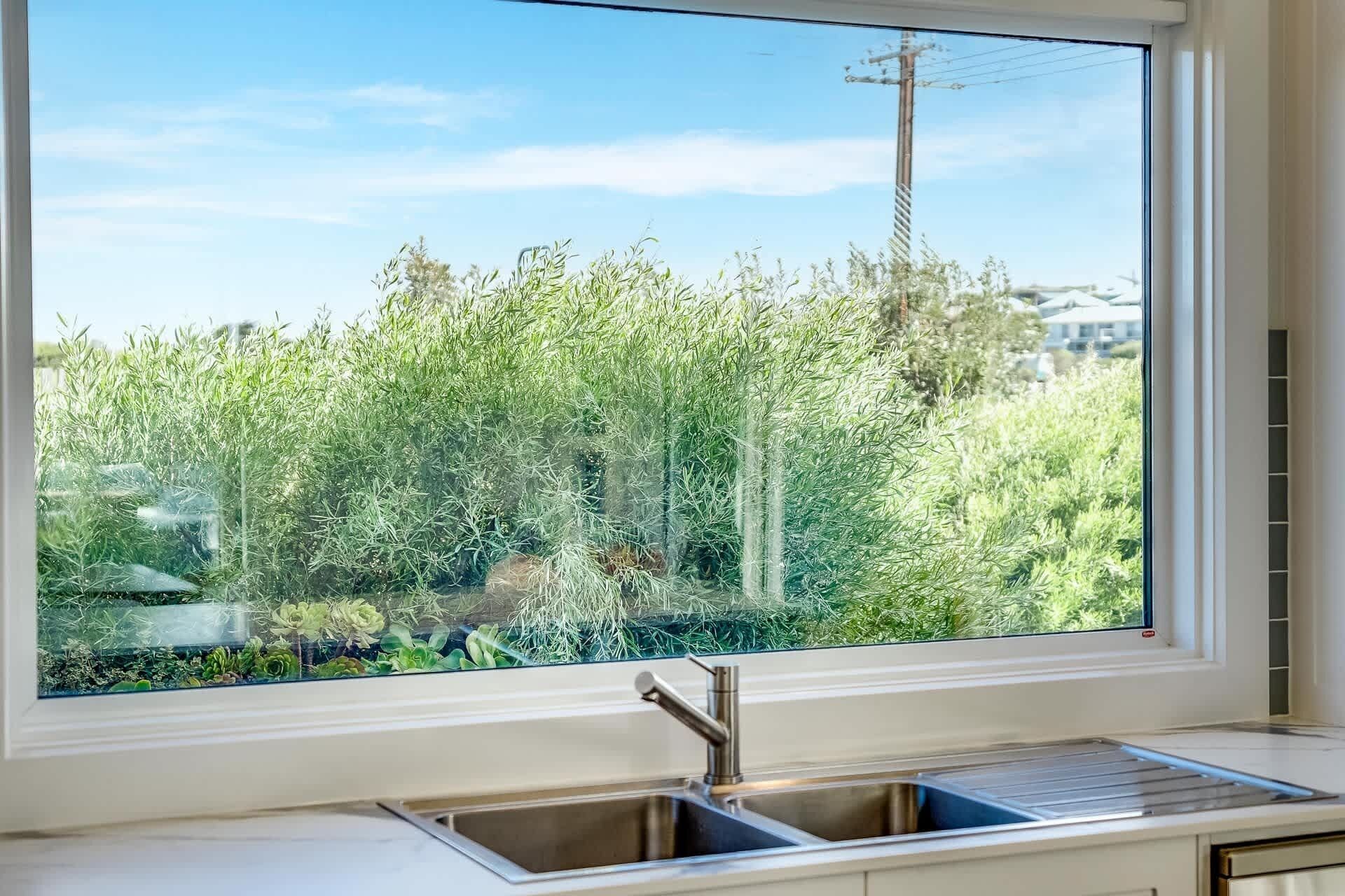 Uma cozinha com pia de aço inoxidável e janela com vista para um jardim.