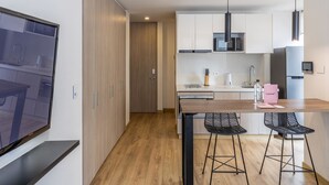 A modern kitchen with wooden cabinets, a microwave, and a refrigerator. There are two black bar stools and a wooden dining table. - w Splendid Loft in Santa Ana (Bogotá)