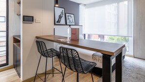 A modern kitchen with a wooden island, two black wireframe chairs, a pendant light, and a large window with a view of buildings. - w Splendid Loft in Santa Ana (Bogotá)