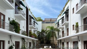 Une piscine avec une terrasse en bois au premier plan, entourée de bâtiments blancs dotés de balcons et de plantes.