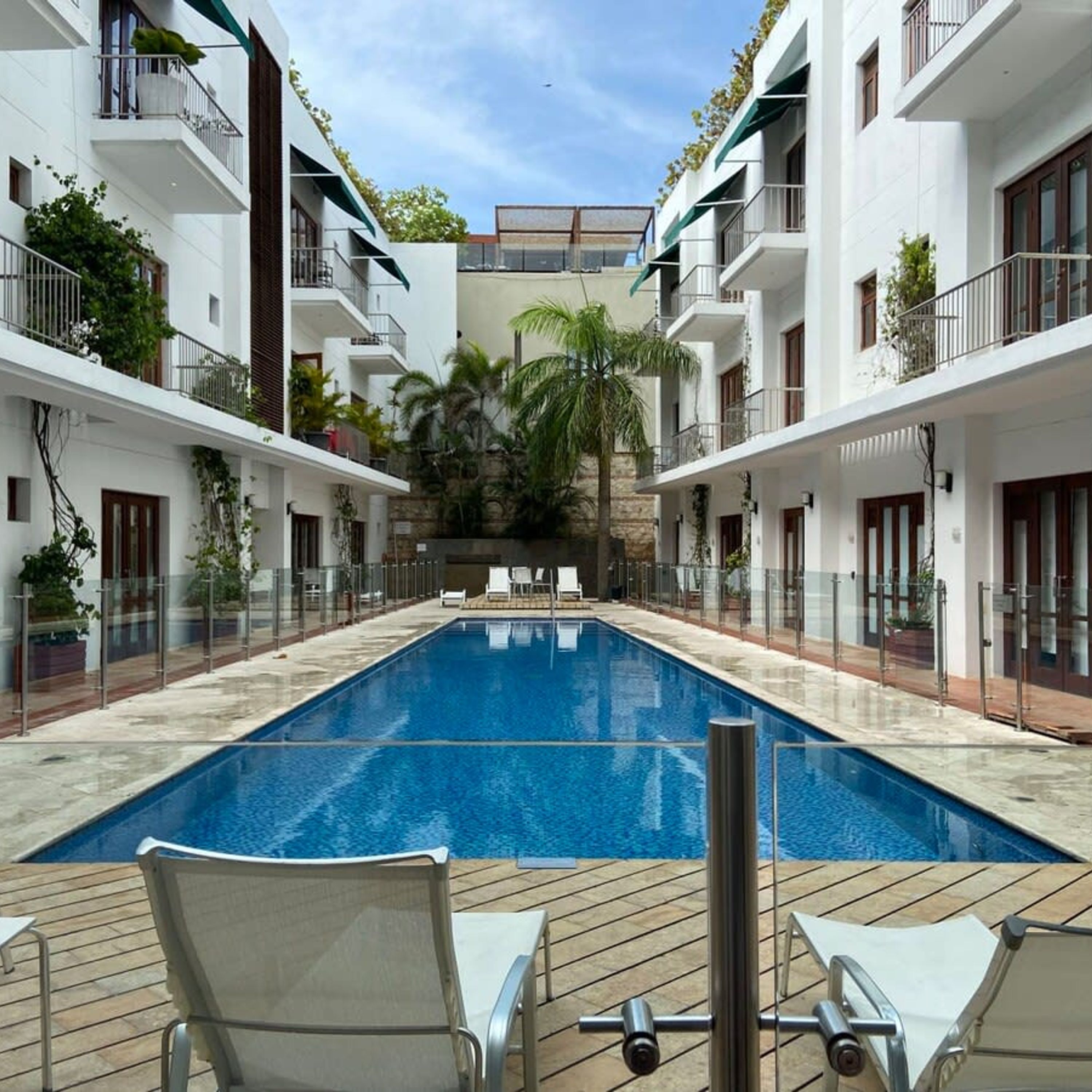 A swimming pool surrounded by white buildings with balconies, some with plants.
