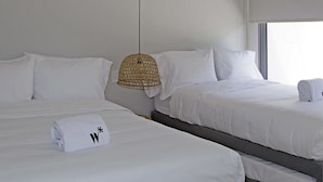 A hotel room with two beds, a woven pendant light, and a large window with blinds.