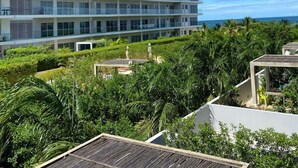 A multi-story hotel with balconies, surrounded by lush greenery and a view of the ocean.