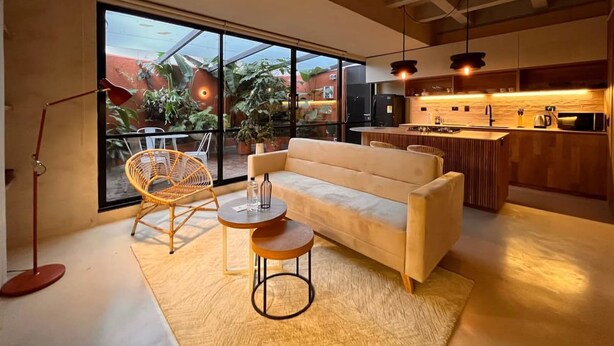A modern living room with a sofa, two chairs, a small table, and a large window overlooking a garden.