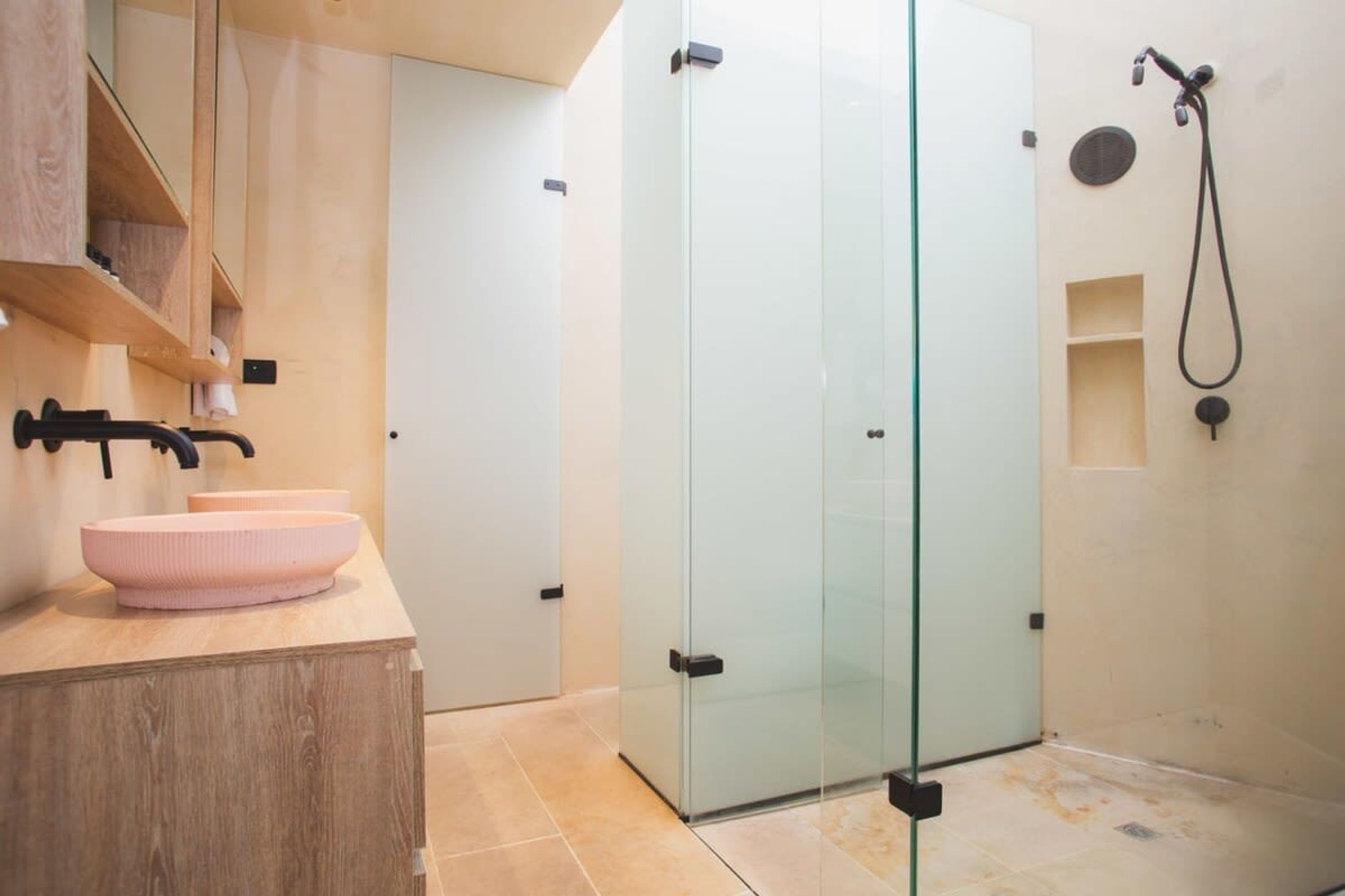 A modern bathroom with a glass-enclosed shower, a wooden vanity with a pink basin, and a towel rack.