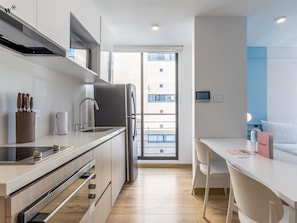 A modern kitchen with a built-in oven, a refrigerator, and a sink. There is a dining area with a table and chairs.