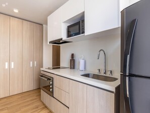A modern kitchen with wooden cabinets, a stainless steel sink, a black refrigerator, and a microwave.