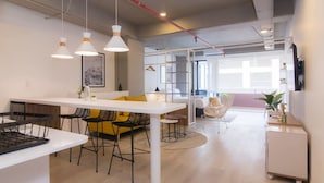 Une cuisine moderne avec un plan de travail blanc, des chaises noires et un canapé jaune. On y trouve une table à manger recouverte d’une nappe blanche et des lampes suspendues.