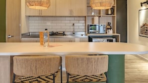 A modern kitchen with a central island, two bar stools, hanging wicker pendant lights, and a visible microwave.