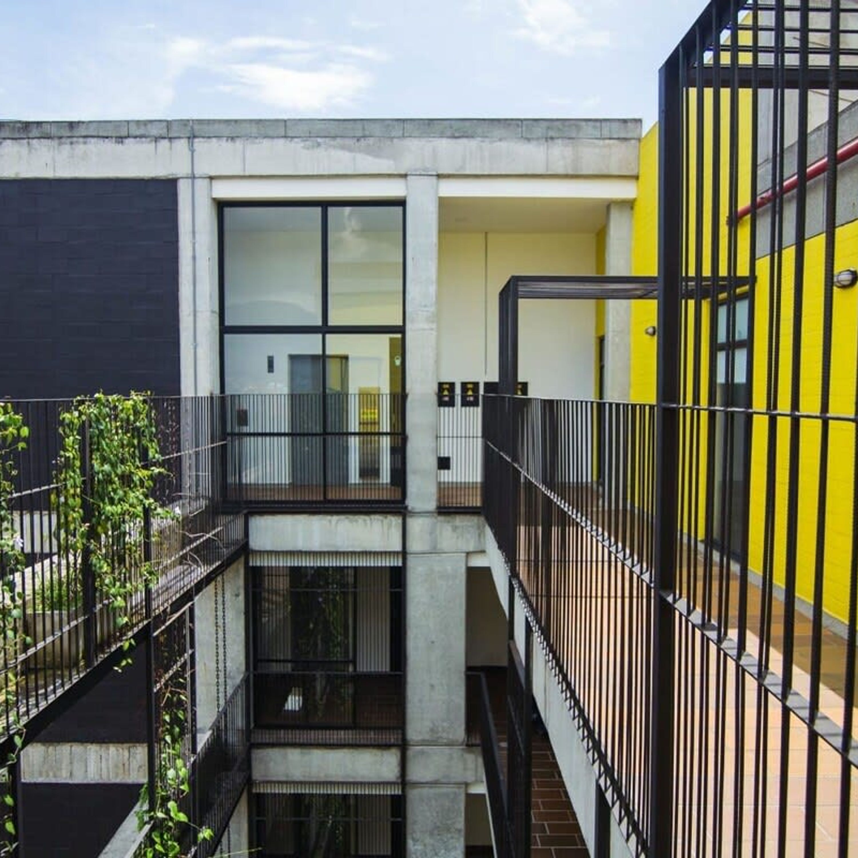 A multi-level building with a concrete facade, large windows, and a yellow section on the right.
