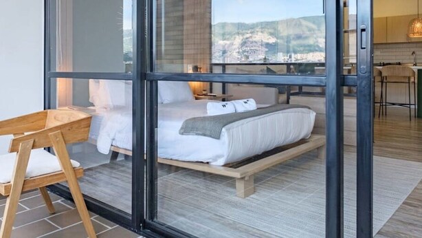 A modern bedroom with a large glass door, a wooden bed frame, and a view of a cityscape.