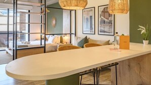 A modern office space with a central island table, hanging wicker lamps, and a green accent wall.