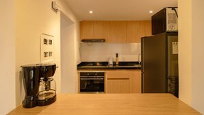Een kleine keuken met houten kastjes, een inbouwoven, een koelkast en een koffiezetapparaat op het aanrecht.