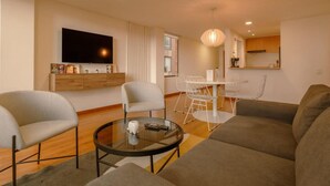 Een moderne woonkamer met een bank, twee fauteuils, een glazen salontafel en een eethoek met een witte tafel en stoelen.