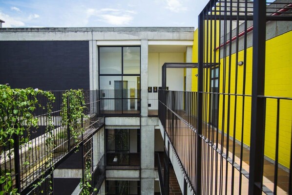 Un edificio de varios niveles con una escalera central, barandales negros y una pared amarilla en un lateral.