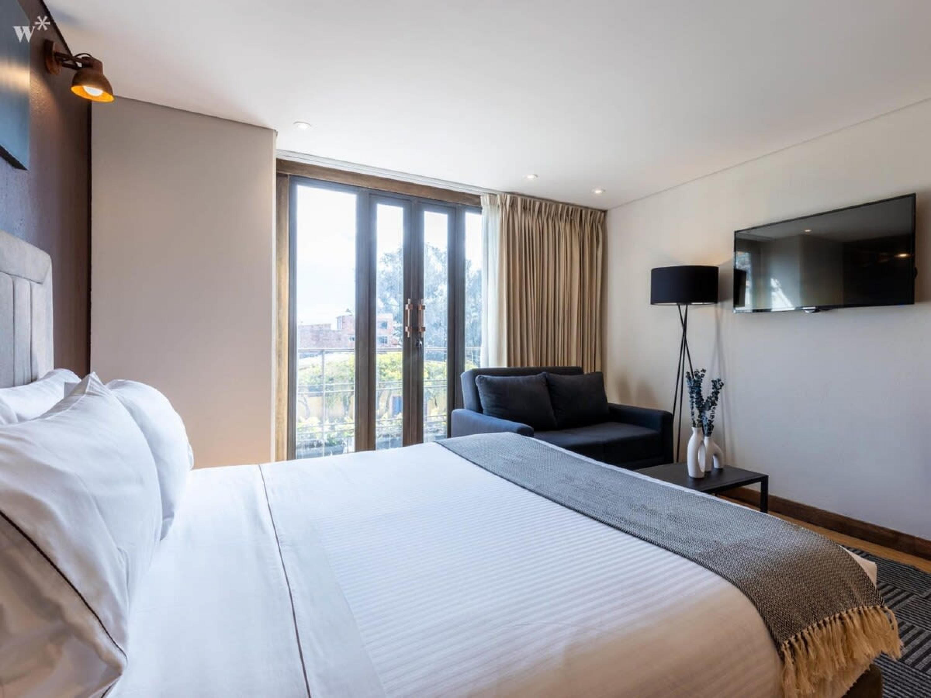 Una habitación de hotel con una cama grande, un sofá, un televisor y una ventana con cortinas.