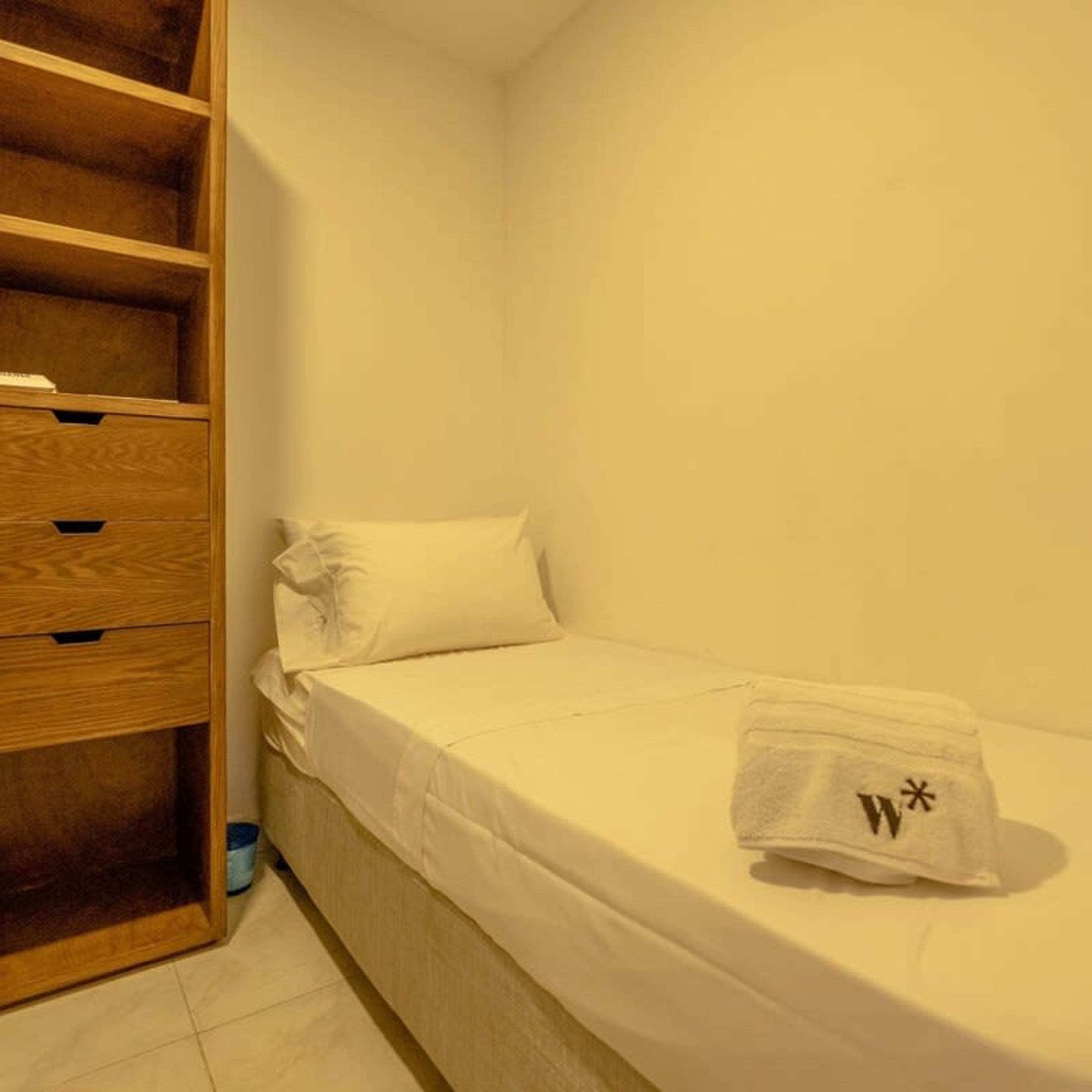 Een kleine eenpersoonskamer met een houten garderobe en nachtkastje.