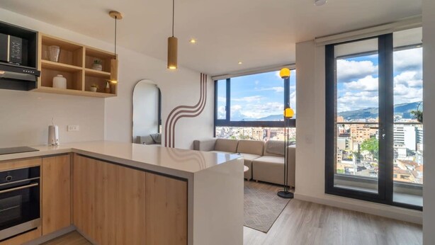 A modern kitchen with wooden cabinets, a built-in oven, and a large window offering a city view. - w Classy 1BR in Chapinero (Bogotá)