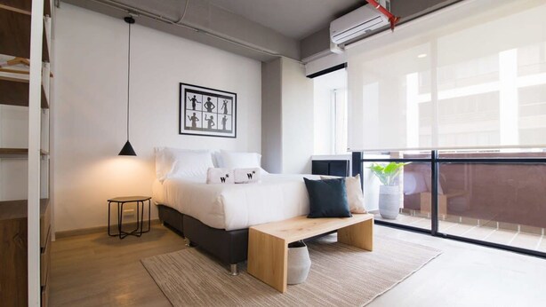 Ein modernes Schlafzimmer mit Bett, Nachttisch, Bank und einem großen Fenster mit Blick.