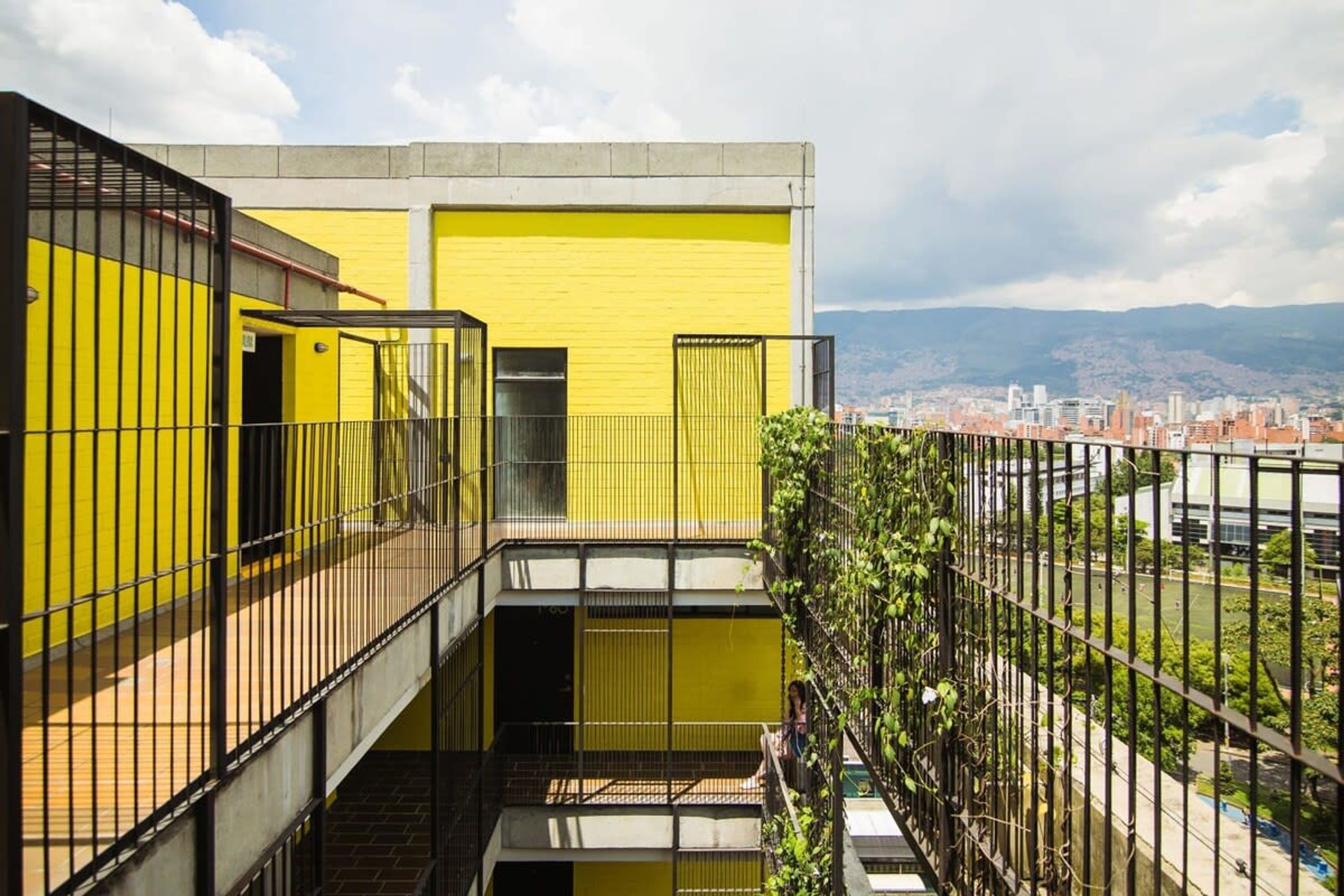 A yellow building with a metal railing and a view of a cityscape in the background.