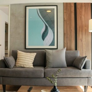 A modern living room with a grey sofa, a framed abstract artwork, and a vase with a plant. - w Dreamy 1BR in Barranco (Lima)