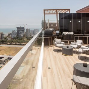 A modern outdoor balcony with a wooden floor, a grill, and seating areas. - w Artistic 1BR in Barranco (Lima)