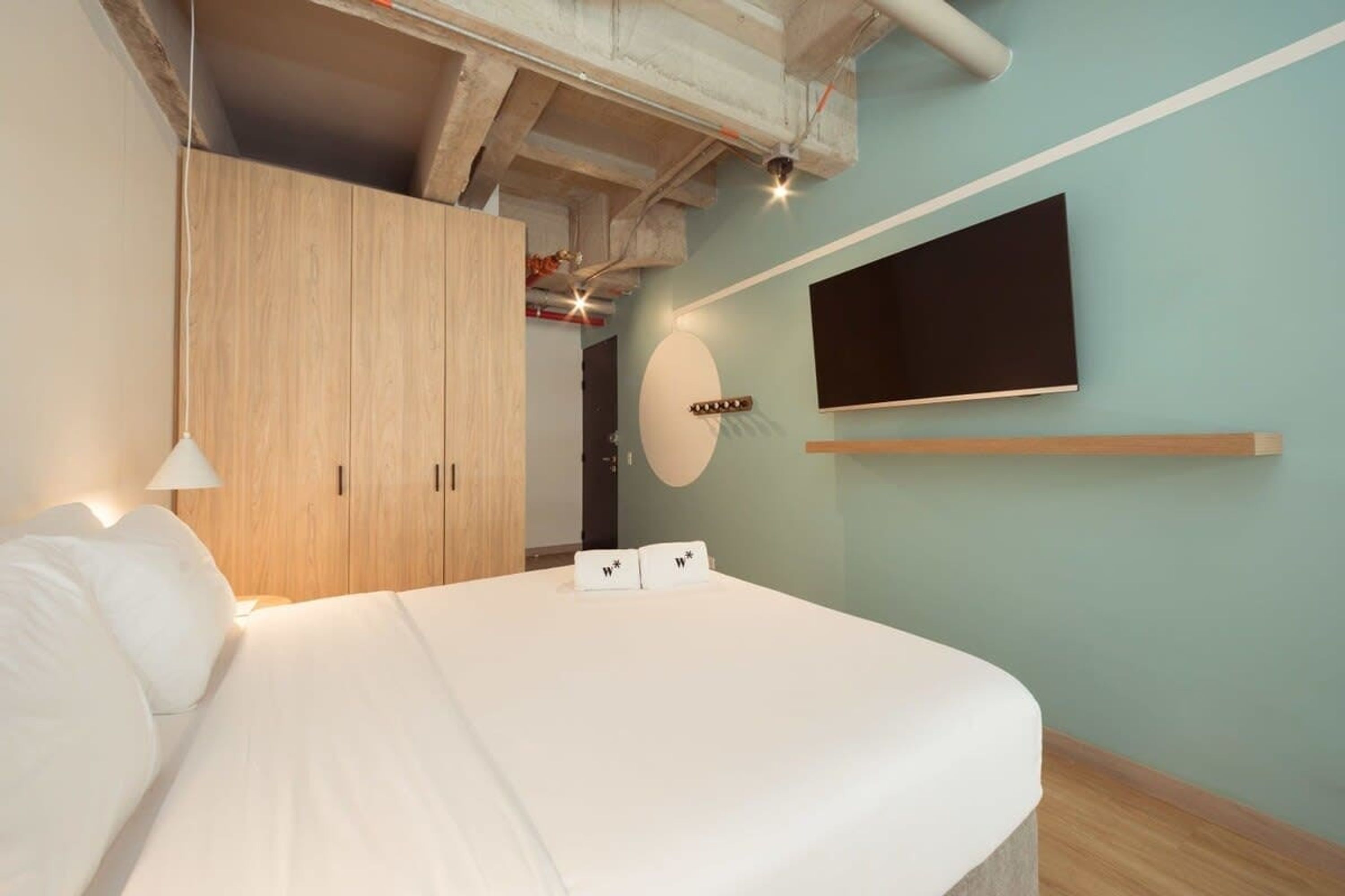 A modern bedroom with a large bed, wooden wardrobe, and a mounted TV.