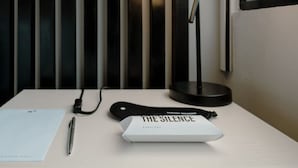 A neatly arranged hotel room with a bed, a bedside table, a lamp, a pen, a notepad, and a box labeled "THE SILENCE EARPLUGS". - Cozy Loft in Country (Bogotá)