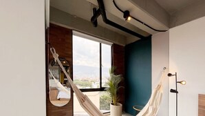A modern room with a hammock, a large window, and a view of the city. - Trendy Loft With Balcony in Laureles (Medellín)