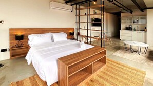 A modern bedroom with a wooden bed, a small desk, and a kitchenette in the background. - Trendy Loft With Balcony in Laureles (Medellín)