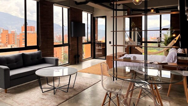 A modern hotel room with large windows, a sofa, a dining table, and a hammock. - Trendy Loft With Balcony in Laureles (Medellín)