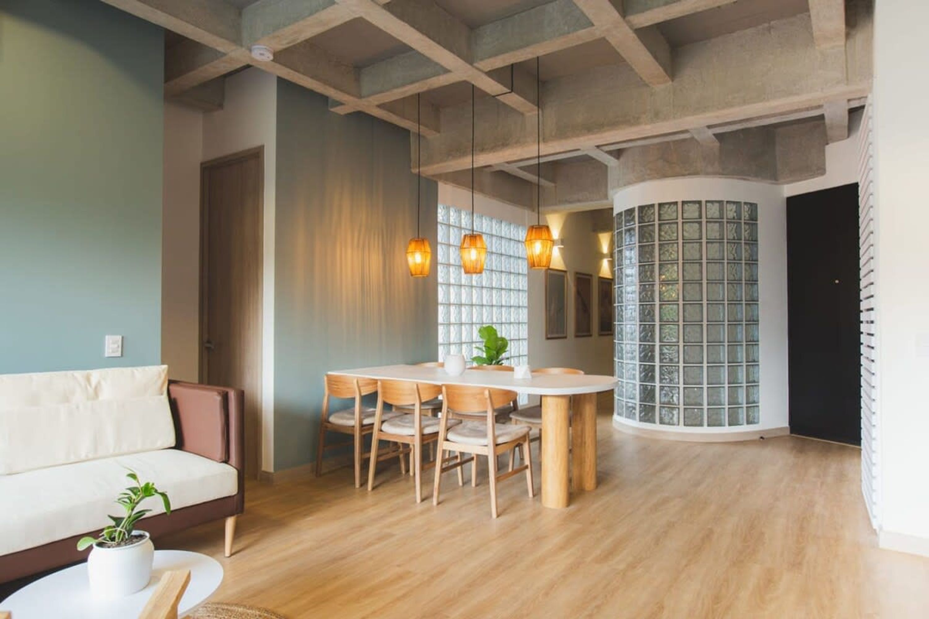 Una sala de estar moderna con una mesa de comedor de madera, sillas, un sofá y lámparas colgantes.