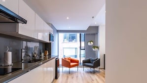 A modern kitchen with a black countertop, white cabinets, and a large window. There are two chairs, one orange and one gray, and a hanging plant. - Perfect Loft in San Patricio (Bogotá)