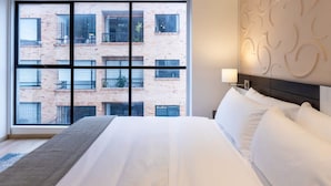 A hotel room with a large window, a bed with white linens, and a decorative wall panel. - Perfect Loft in San Patricio (Bogotá)