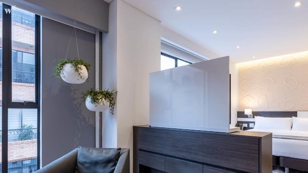 A modern hotel room with a grey sofa, a large bed, and a wall-mounted TV. - Perfect Loft in San Patricio (Bogotá)