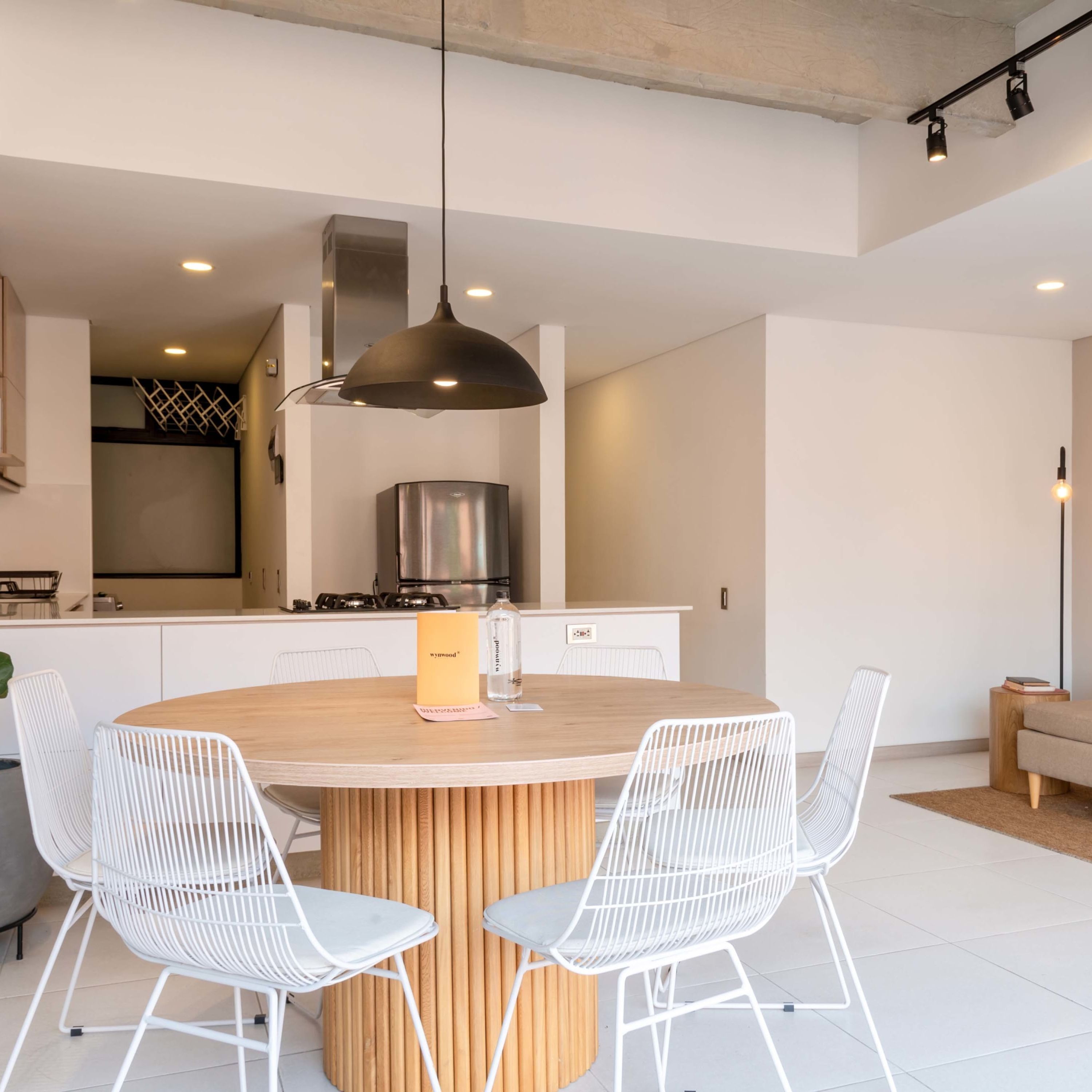 A modern kitchen with a round wooden table, white wire chairs, and a pendant light.
